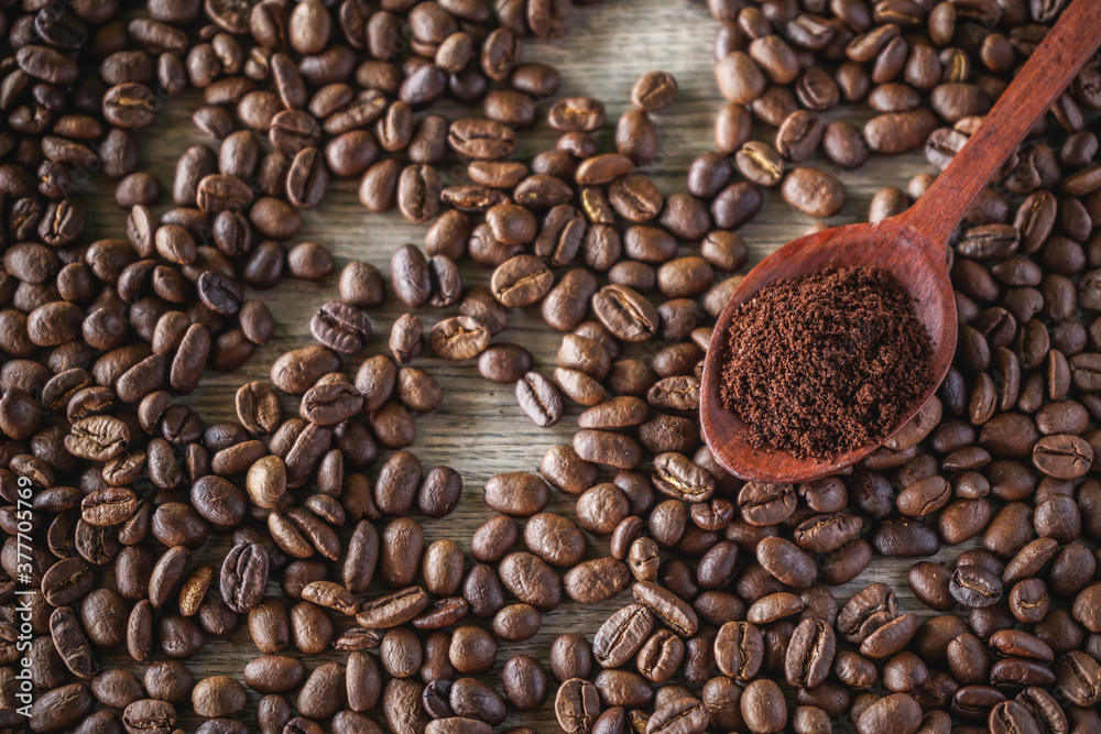 ground coffee in wooden spoon with Roasted coffee beans background 