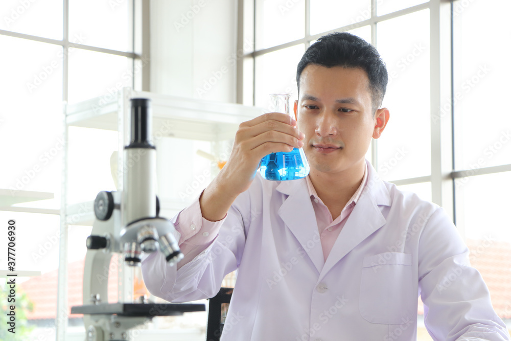 An Asian scientist or chemist looks at a blue liquid chemical test tube in the laboratory.