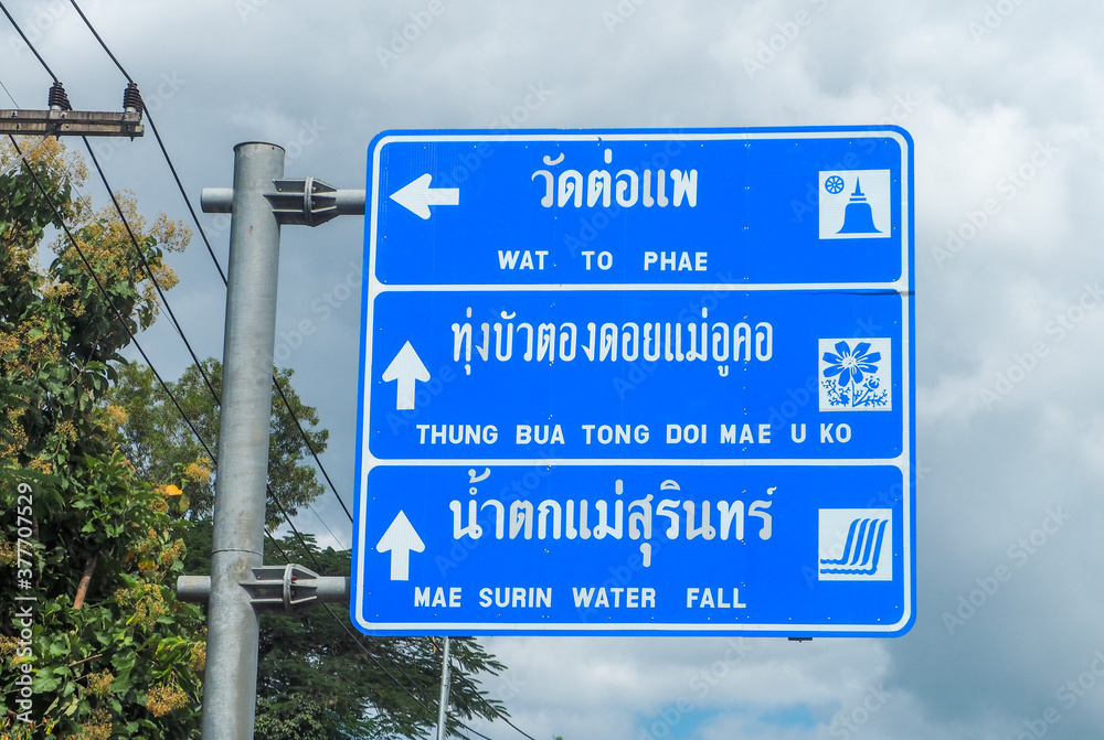 The blue sign tells the name of the tourist attractions in Mae Hong Son Province, Thailand, painted in white in Thai and English, reads Wat To Phae, Thung Bua Tong, Doi Mae Ukho, Mae Surin Waterfall.