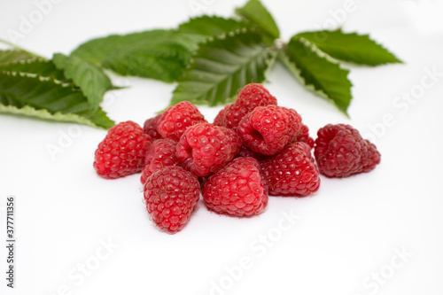 Ripe berries of red raspberries with green leaves on a white background