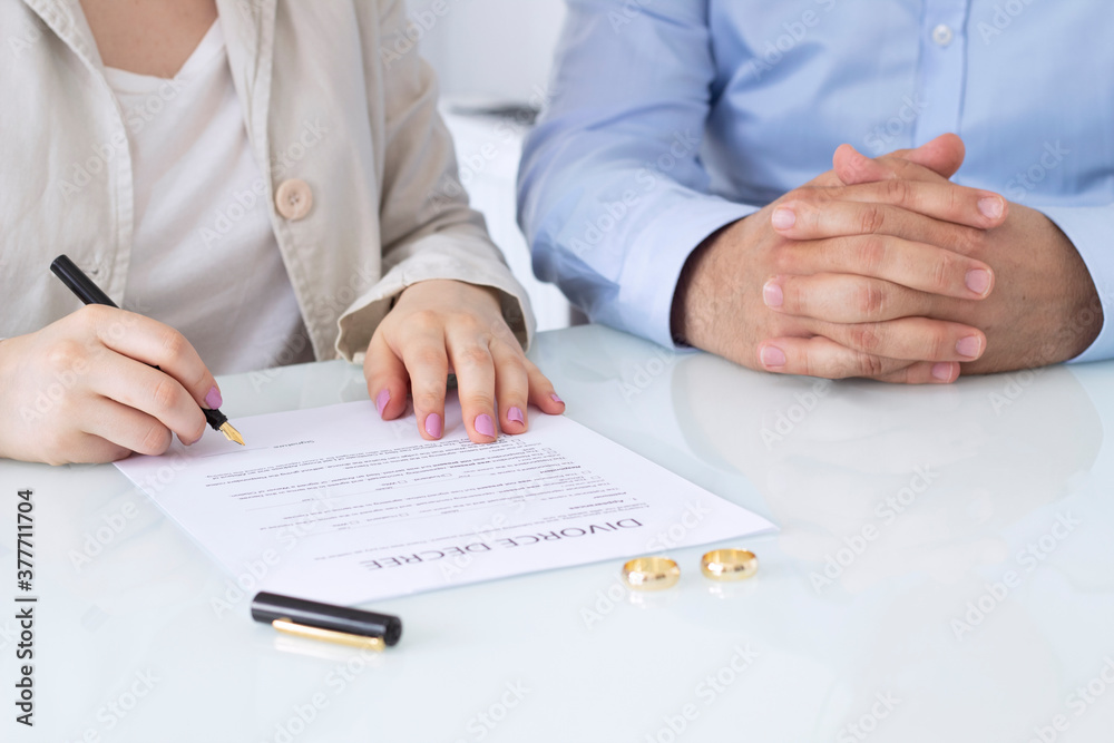 Hands of wife, husband signing decree of divorce, dissolution, canceling marriage, legal separation documents, filing divorce papers or premarital agreement prepared by lawyer. Wedding ring Hands of wife, husband signing decree of divorce, dissolution, canceling marriage, legal separation documents, filing divorce papers or premarital agreement prepared by lawyer. Wedding ring
