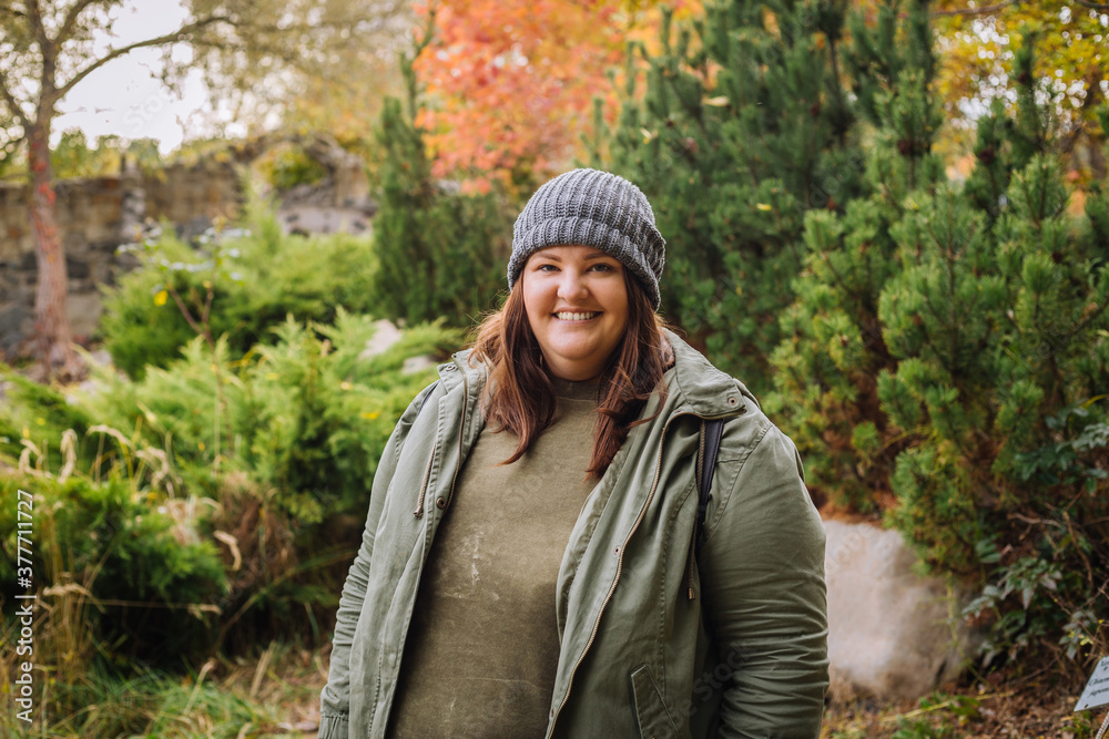 Young cheerful curvy woman in grey hat and green jacket walking in the park Young cheerful curvy woman in grey hat and green jacket walking in the park