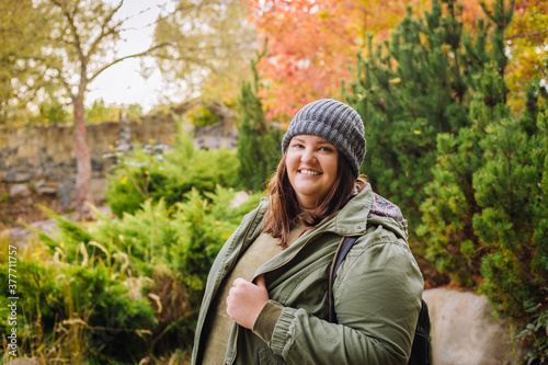 Young  cheerful curvy woman in grey hat and green jacket walking in the park