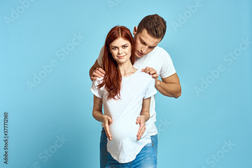 Pregnant woman in white t-shirt and man married couple waiting for baby blue background cropped view of emotions
