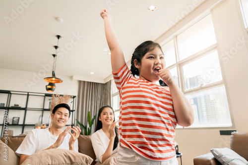 happiness pleasure asian lovely family enjoy watch and cheer up little daughter girl singing and dance practice in front of tv in living room