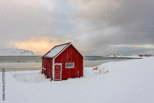 Lofoten Islands in Norway and their beautiful winter scenery at sunset. Idyllic landscape with red house on snow covered beach. Tourist attraction in the arctic circle.