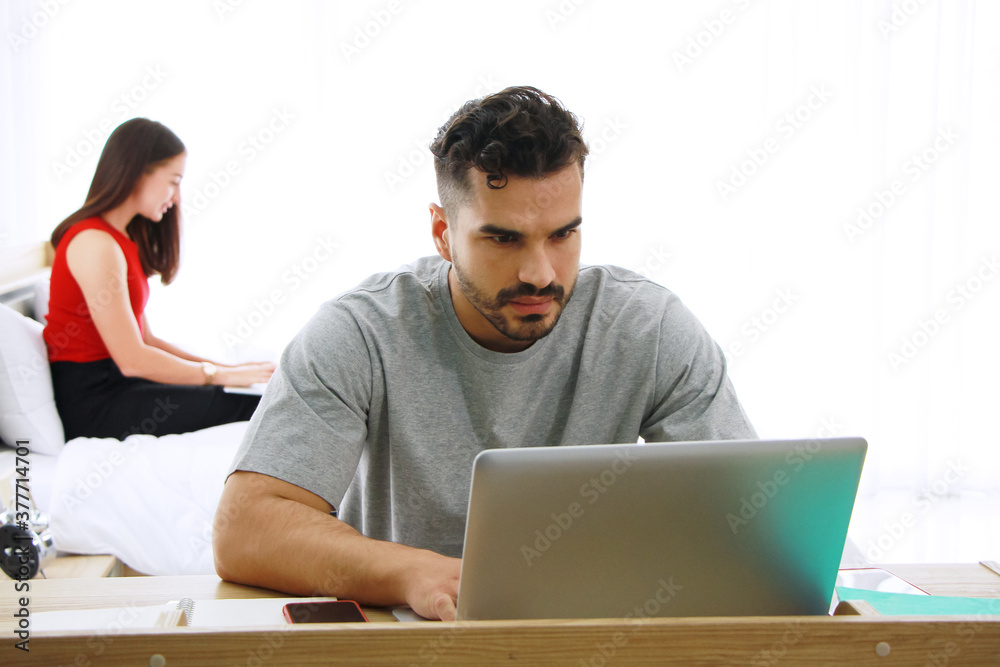 Serious Caucasian male working with laptop and girlfriend relaxing for shopping online in social media with notebook in bedroom together. Technology and lifestyle on holiday of family Concept. Serious Caucasian male working with laptop and girlfriend relaxing for shopping online in social media with notebook in bedroom together. Technology and lifestyle on holiday of family Concept.