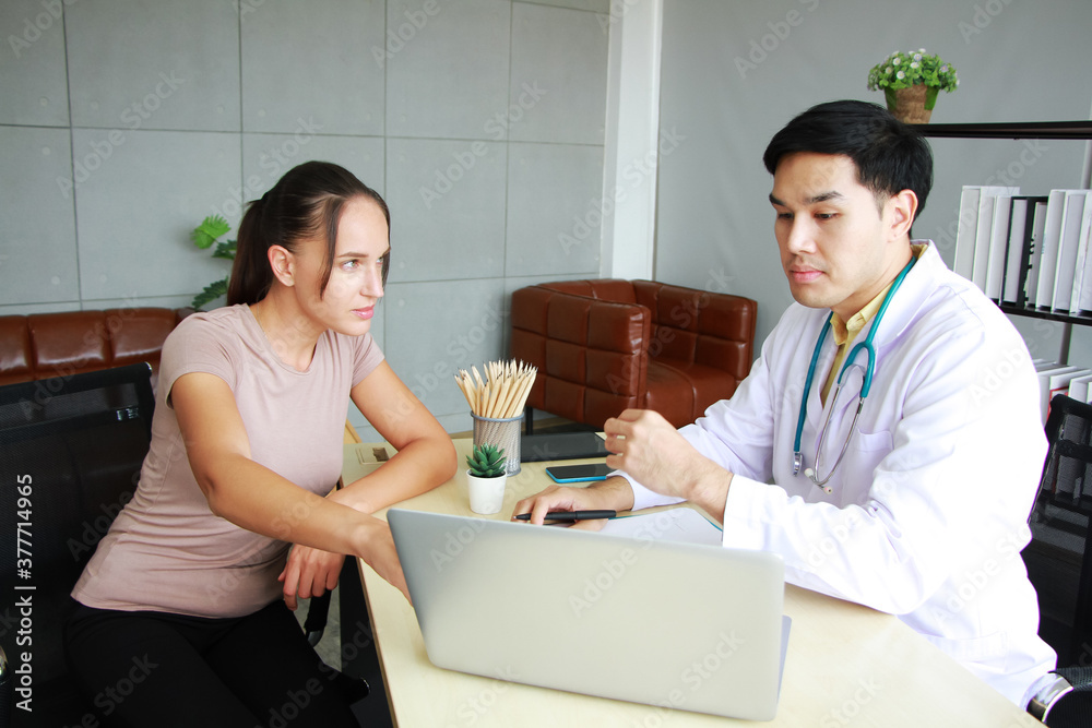 Young Asian male psychiatrist is specialist in psychiatry Caucasain female Patient serious together for therapy and talking for encourage with laptop in Clinical treatment for emotional symptoms. Young Asian male psychiatrist is specialist in psychiatry Caucasain female Patient serious together for therapy and talking for encourage with laptop in Clinical treatment for emotional symptoms.