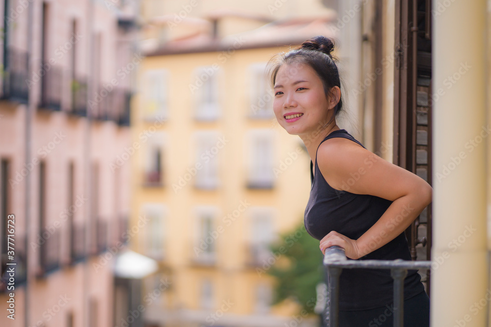 young happy and beautiful Asian Korean woman in hair bun enjoying city view from hotel room balcony in Spain during holidays trip in Europe smiling cheerful in urban background