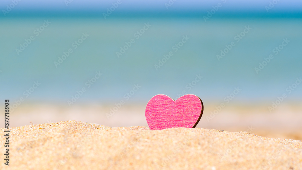 Pink heart on a sandy beach against the background of the sea. Vacation concept by the sea Pink heart on a sandy beach against the background of the sea. Vacation concept by the sea