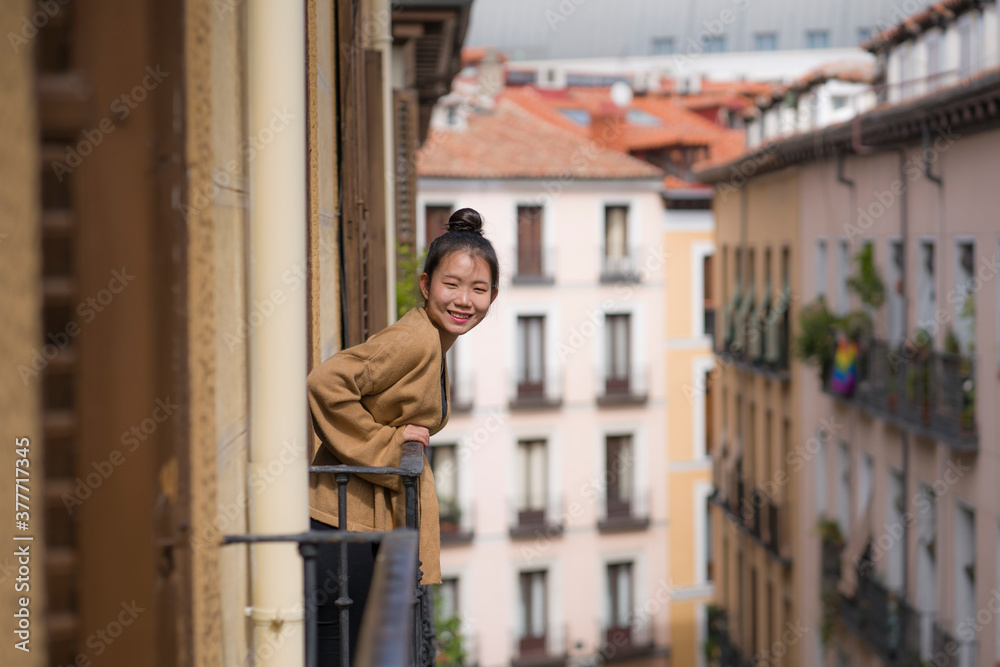 young happy and beautiful Asian Japanese woman in hair bun enjoying city view from hotel room balcony in Spain during holidays trip in Europe smiling cheerful