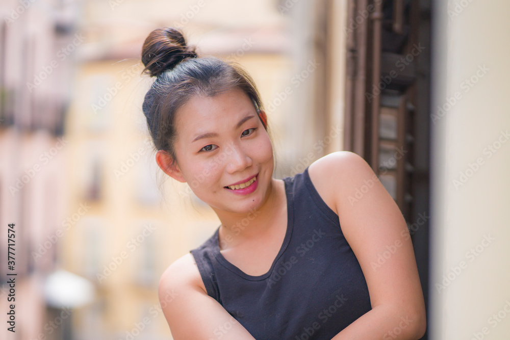 young happy and beautiful Asian Japanese woman in hair bun enjoying city view from hotel room balcony in Spain during holidays trip in Europe smiling cheerful