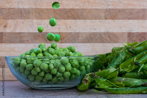 Freshly shelled garden peas striaght from the pea pods falling into a glass bowl  with the disgarded husks photo