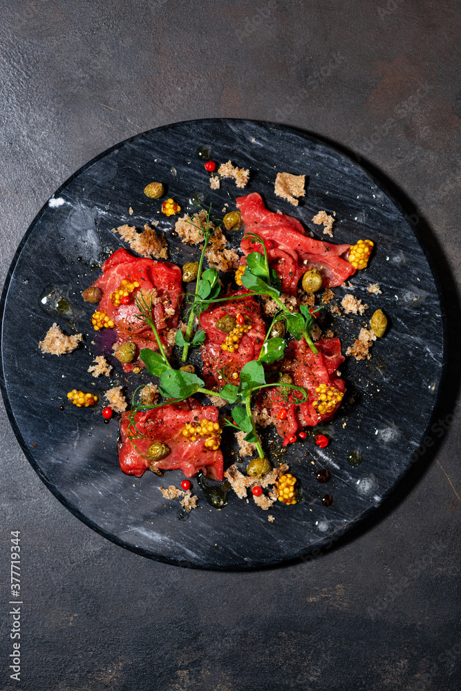 fresh beef carpaccio with capers and arugula, vertical top view fresh beef carpaccio with capers and arugula, vertical top view