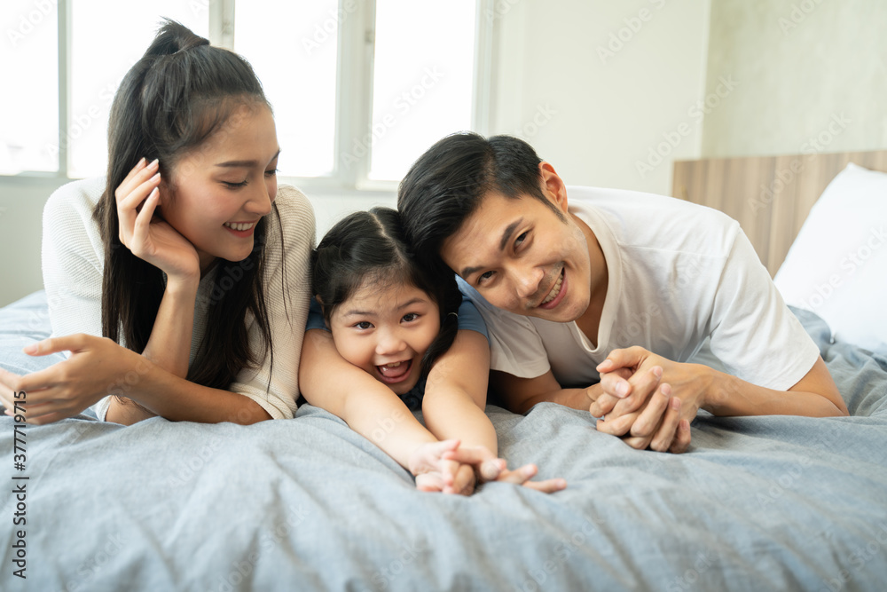 happy asian family in the bedroom.young asian parents kissing their daughter while lying on bed. happy asian family in the bedroom.young asian parents kissing their daughter while lying on bed.