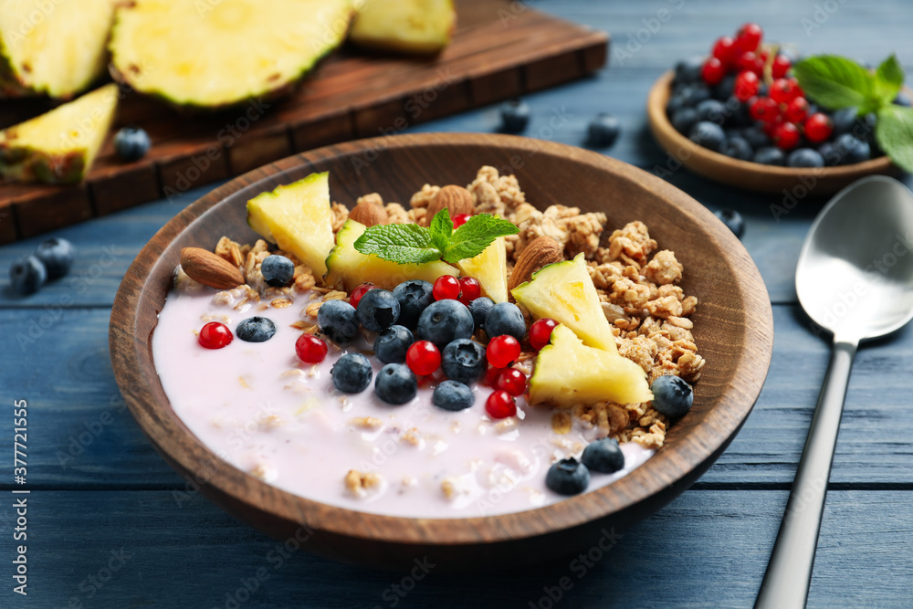 Tasty granola with yogurt, berries and sliced pineapple served for breakfast on blue wooden table Tasty granola with yogurt, berries and sliced pineapple served for breakfast on blue wooden table