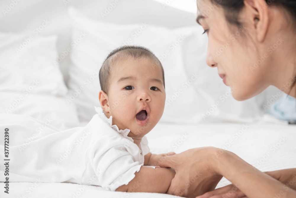 Beautiful asian mother and baby are playing on white bed and looking at each other. Happy asia mother and infant lying on bed at home. Beautiful asian mother and baby are playing on white bed and looking at each other. Happy asia mother and infant lying on bed at home.