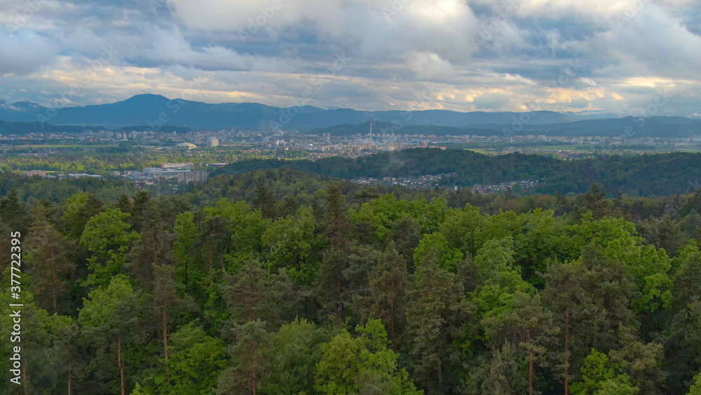 AERIAL: Golden sunbeams shine through grey clouds and onto the city of Ljubljana