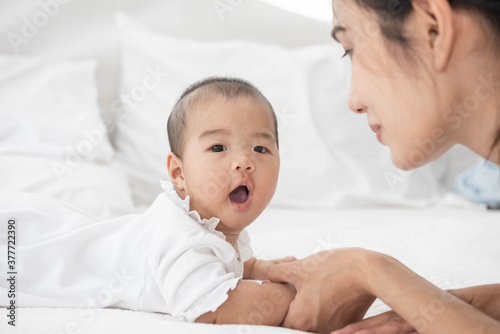 Beautiful asian mother and baby are playing on white bed and looking at each other. Happy asia mother and infant lying on bed at home.