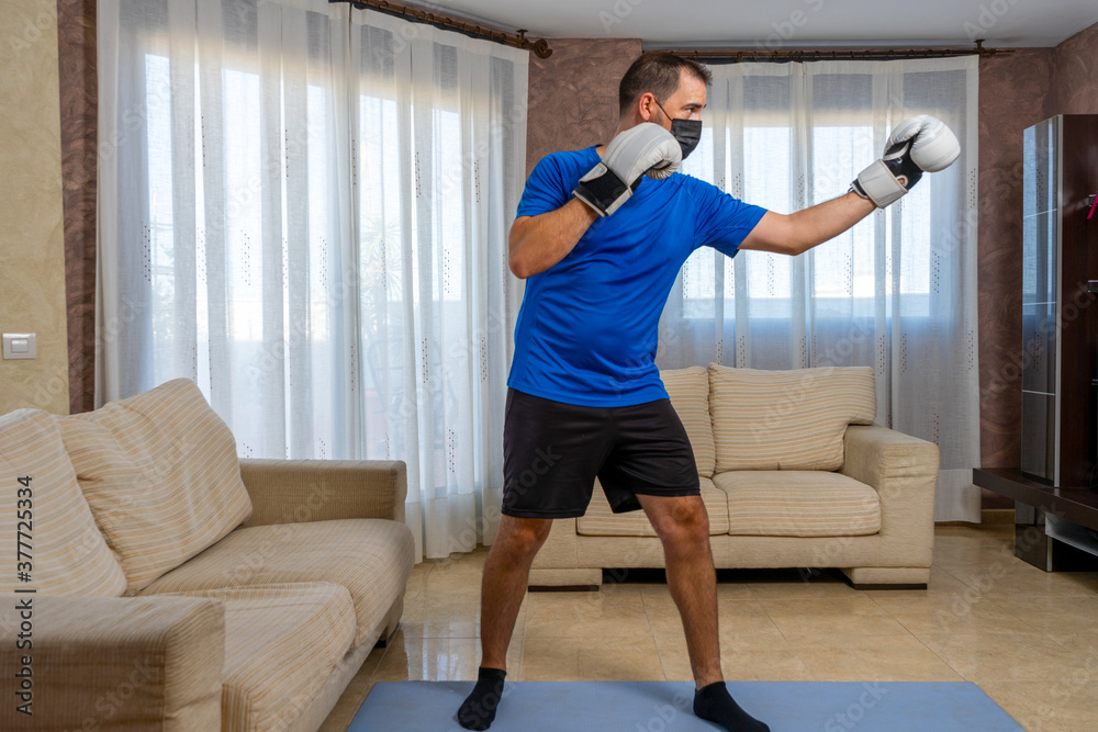 Fit bearded man dressed in black and blue sportswear practicing martial arts in his living room