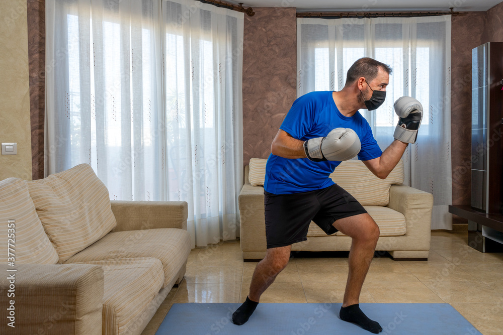 Fit bearded man dressed in black and blue sportswear practicing martial arts in his living room