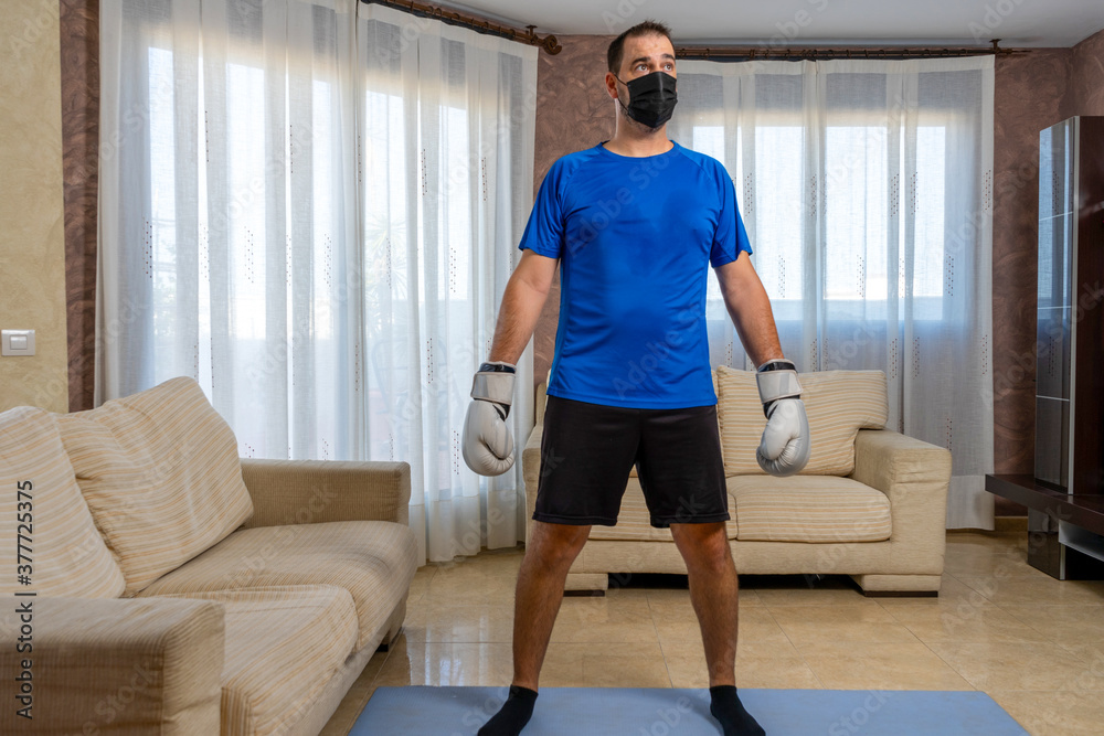 Fit bearded man dressed in black and blue sportswear practicing martial arts in his living room Fit bearded man dressed in black and blue sportswear practicing martial arts in his living room