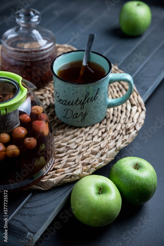 Turquoise mug with tea. Glass teapot with berry tea. Green apple. Still life on a dark table.