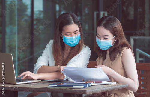 Two business women wearing masks and working together