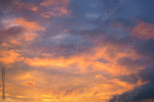 Cloudy sky at sunset. Dark purple and yellow natural background or wallpaper. The rays of the setting sun effectively illuminate the clouds. Beautiful and spectacular evening skies