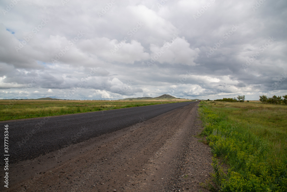 Fototapeta premium View of the track in a field with hills and dark clouds.