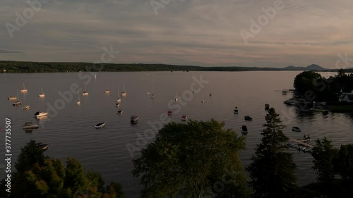 Drone Flying Over The Scenic Lake Memphremagog With Floating Boats Scattered By The Beachfront At Sunset In Magog, Quebec, Canada - Aerial Shot (Panning) photo