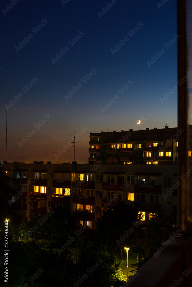 Fototapeta premium Waxing crescent moon rising over apartment blocks at nightfall, urban view, cityscape