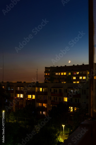 Waxing crescent moon rising over apartment blocks at nightfall, urban view, cityscape