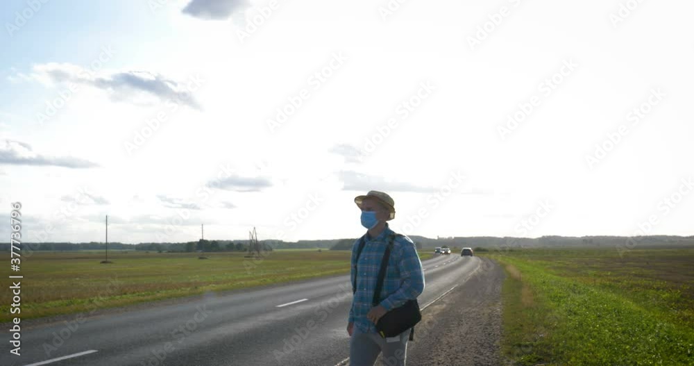 A young man is hitchhiking around the country. The man is trying to catch a passing car for traveling. The man with the backpack went hitchhiking to south. A young man is hitchhiking around the country. The man is trying to catch a passing car for traveling. The man with the backpack went hitchhiking to south.