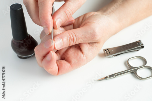 Woman hands doing manicure. Female hands  holding nail file  with nail polish  scissors and nail clippers on white background.