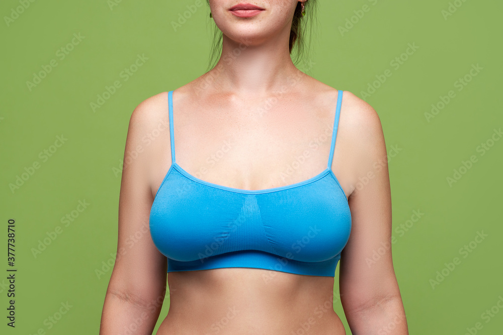 Foto de Woman in blue top bra with big natural breasts on green background  do Stock