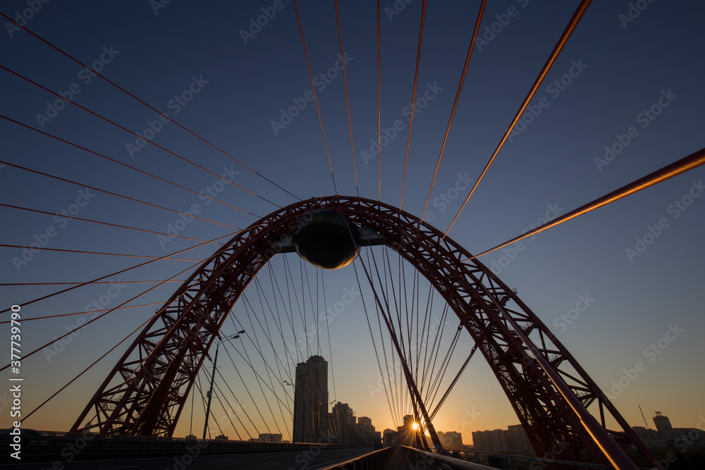 Obraz premium Arched cable-stayed bridge in Moscow, Russia. The backlight of starburst rising sun. No cars or people. High contrast. Clear sky.