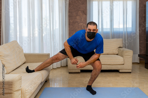 Low-bearded man exercising with black and blue sportswear and mask to prevent coronavirus