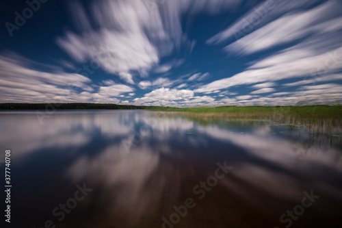 Obraz na plátně Long exposure shot of a lake reflecting blurred clouds moving to the centre of a frame