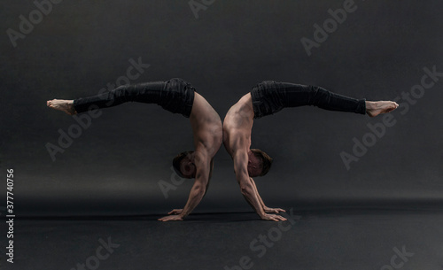 two twin brothers in black jeans with a naked torso perform acrobatic elements, black background
