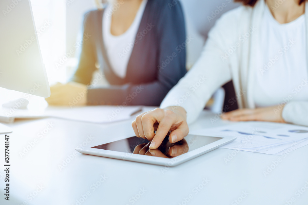 Businesswoman pointing at tablet computer screen while giving presentation to her female colleague. Group of business people working at the desk in office. Teamwork concept Businesswoman pointing at tablet computer screen while giving presentation to her female colleague. Group of business people working at the desk in office. Teamwork concept