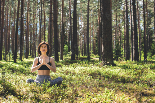 Woman practicing yoga in forest with namaste behind the back. fitness lifestyle at the outdoors nature background. Sunny day in pine forest. copy space