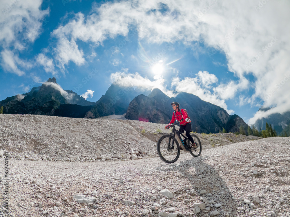 Fototapeta premium pretty senior woman riding her electric mountainbike in the Innerfeld Valley in the Sexten Dolomites near village of Innichen , Tre cime National park, South Tirol, Italy