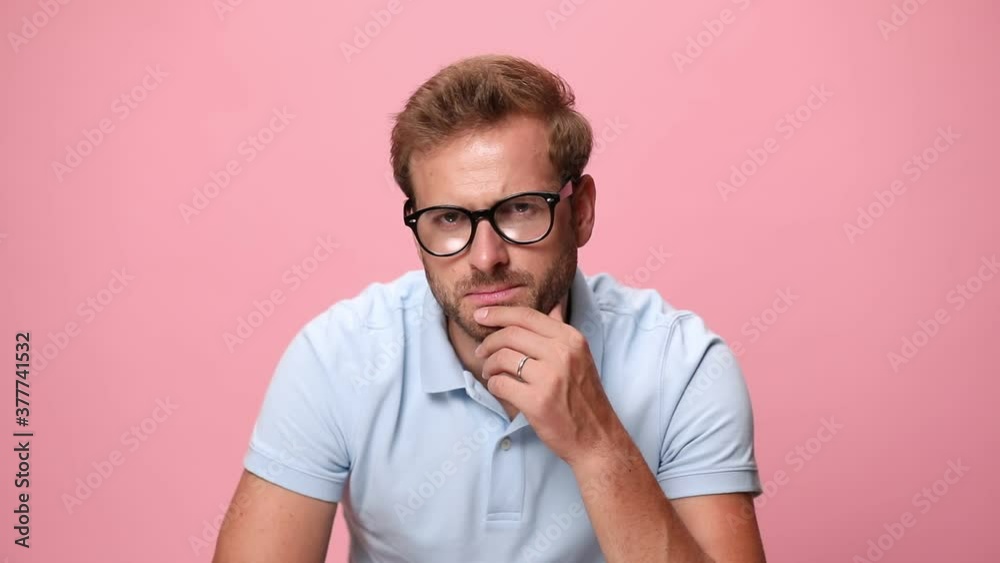 sexy young casual man in blue polo shirt touching sensually chin and thinking, fixing glasses and looking to side, smiling and flirting on pink background sexy young casual man in blue polo shirt touching sensually chin and thinking, fixing glasses and looking to side, smiling and flirting on pink background