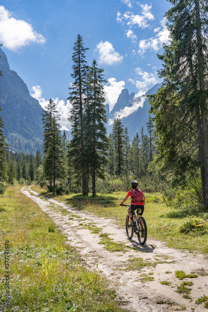 pretty senior woman riding her electric mountainbike in the Fischlein Valley in the Sexten Dolomites wit famous Sextan sundial in background, Tre cime National park, South Tirol, Italy pretty senior woman riding her electric mountainbike in the Fischlein Valley in the Sexten Dolomites wit famous Sextan sundial in background, Tre cime National park, South Tirol, Italy