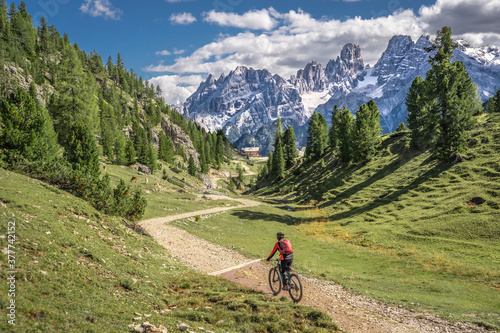 nice and active senior woman riding her electric mountain bike on the high plateau of Pratto Piazzo in the three peaks Dolomites , rocky silhouette of Mount Cristallo in background, South Tirol, Italy