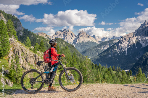 nice and active senior woman riding her electric mountain bike on the high plateau of Pratto Piazzo in the three peaks Dolomites   rocky silhouette of Mount Cristallo in background  South Tirol  Italy
