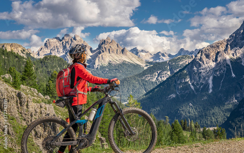 nice and active senior woman riding her electric mountain bike on the high plateau of Pratto Piazzo in the three peaks Dolomites , rocky silhouette of Mount Cristallo in background, South Tirol, Italy © Uwe