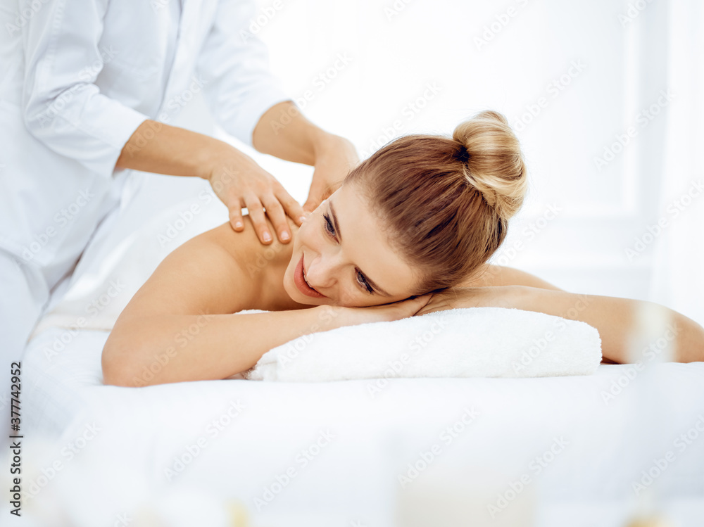Young and blonde woman enjoying massage of back in spa salon. Beauty concept Young and blonde woman enjoying massage of back in spa salon. Beauty concept