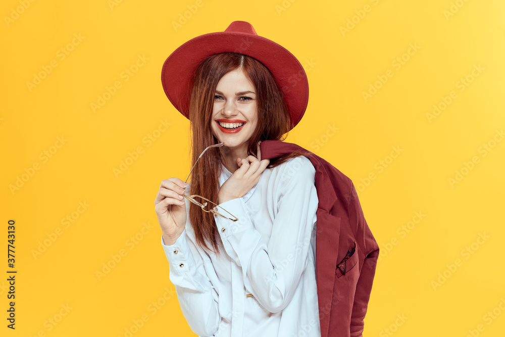 Woman with a jacket on her shoulders red hat white shirt elegant style yellow background Woman with a jacket on her shoulders red hat white shirt elegant style yellow background